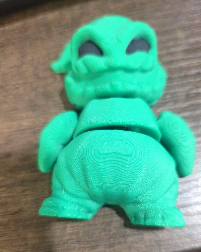 A small green articulated Oogie Boogie figure on a wood surface.