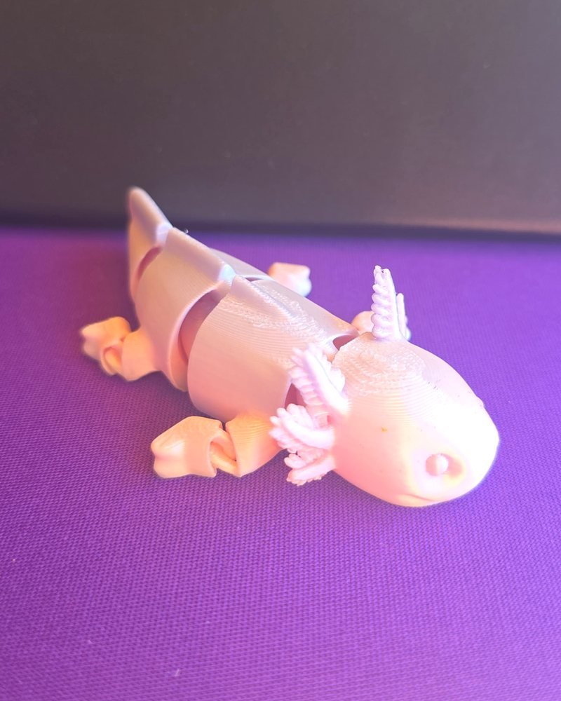 A small pink articulated axolotl with feathery gills, on purple cloth.