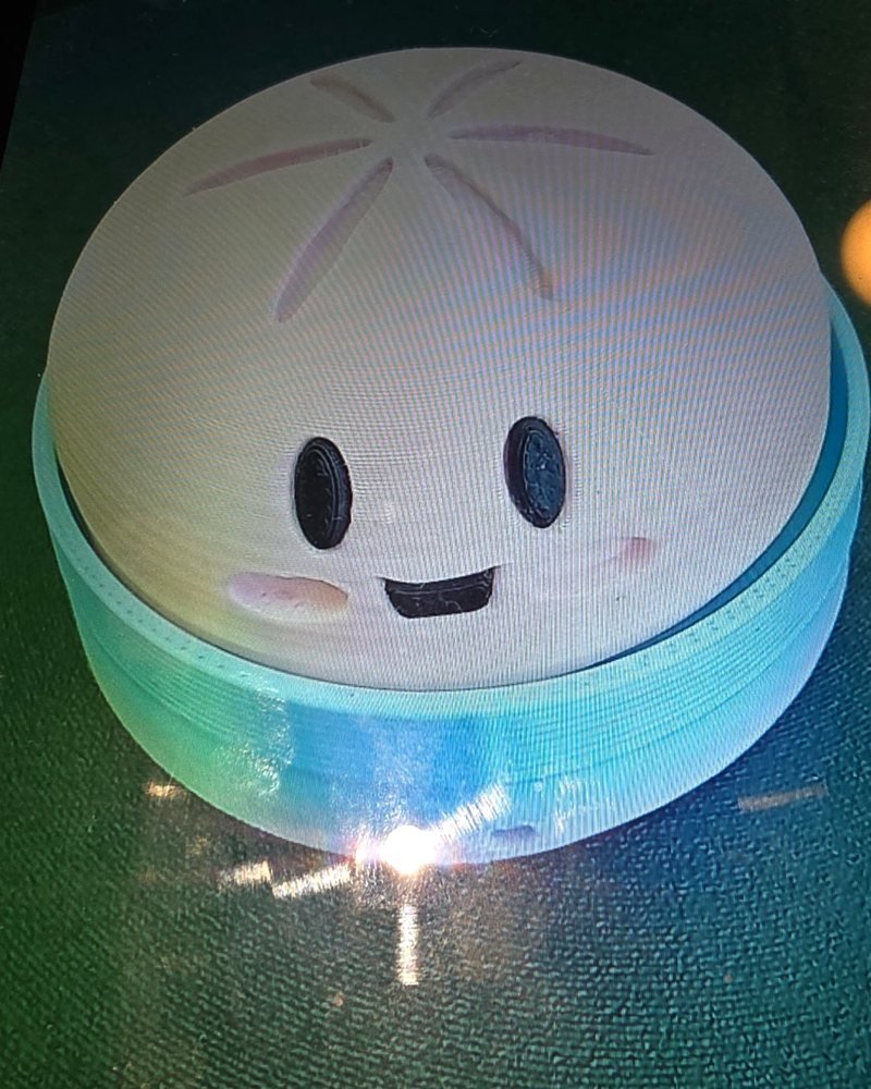 A round lidded box printed to look like a smiling steamed bun, in white with a blue-green base.