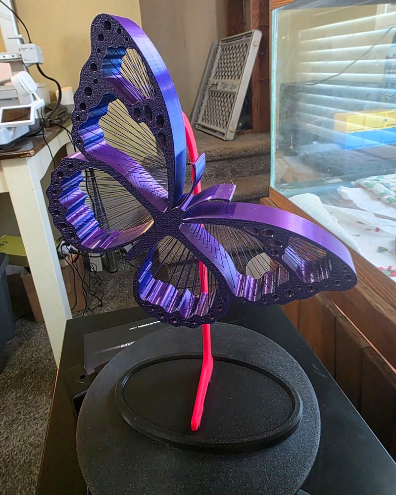 A large purple iridescent butterfly sculpture with strung, open wings, mounted on a stand.