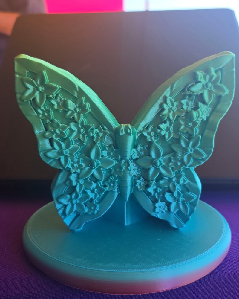 A teal and green butterfly with flower-patterned wings, standing on a round base.