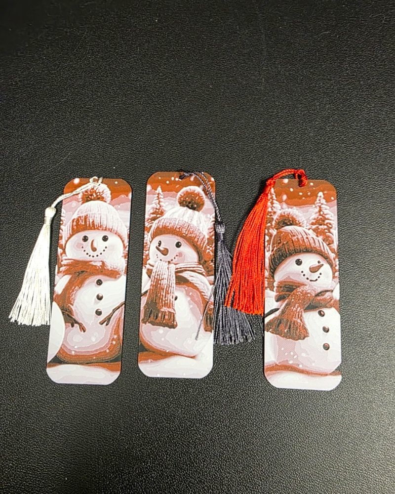 Three Christmas bookmarks printed with a smiling snowman design, each with a tassel.
