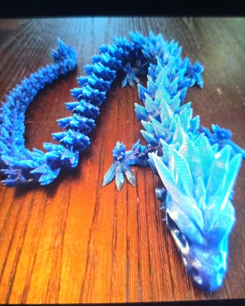 Two articulated dragons with crystalline scales, one deep cobalt and one pale translucent blue, on wood.