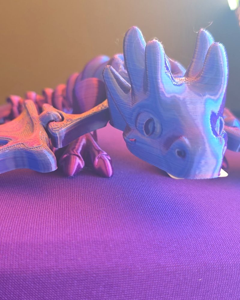 A purple and blue silk-filament dragon lying low with spread wings and a horned head, on purple cloth.
