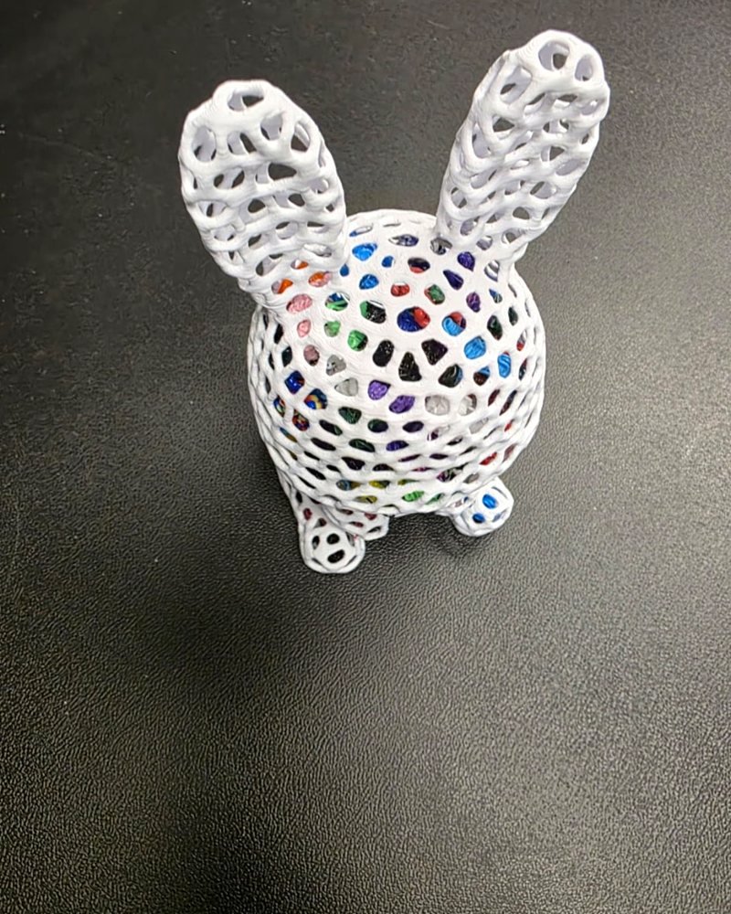 A white lattice-bodied bunny figurine with tall ears, filled with colorful filament scraps.