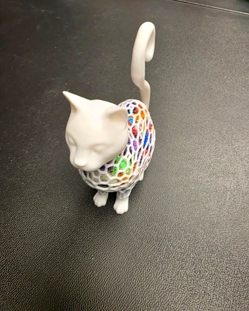 A white lattice-bodied cat figurine with colorful filament scraps visible through the openwork.