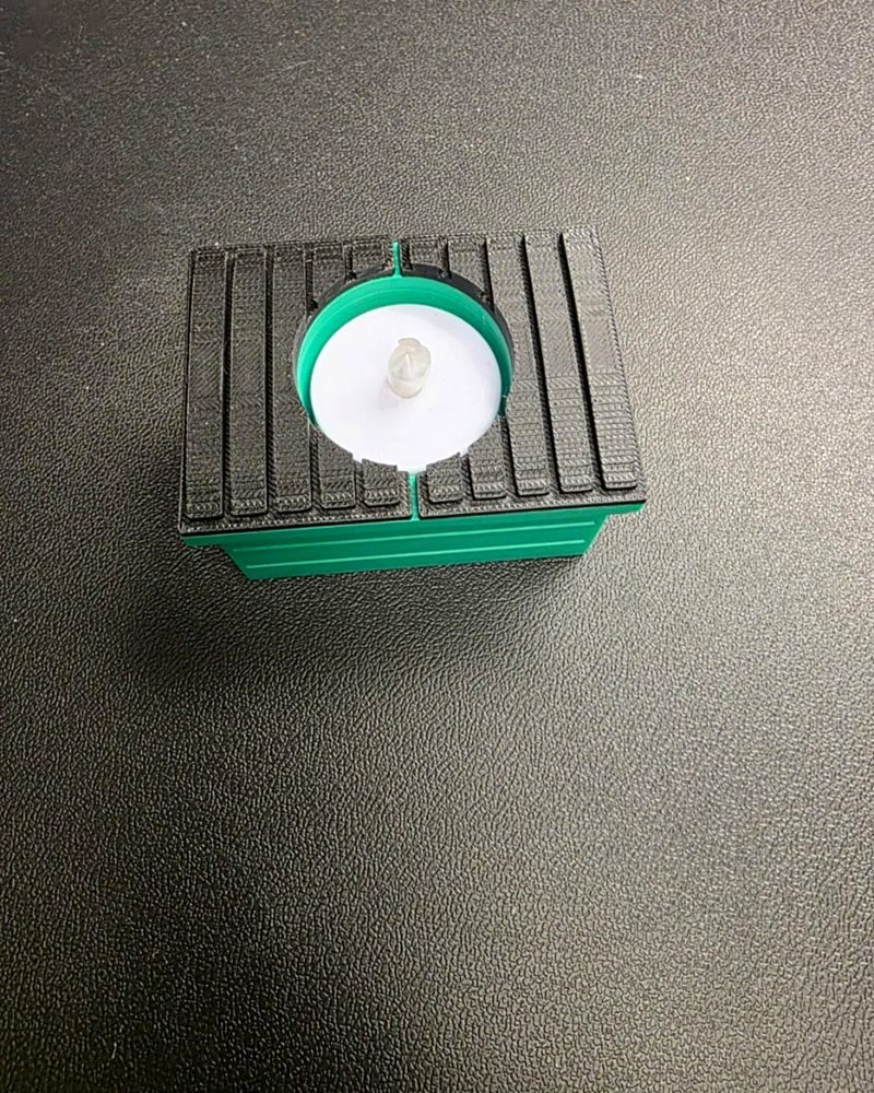 A small ribbed dumpster-shaped tea light holder with a green lid, on a wood table.