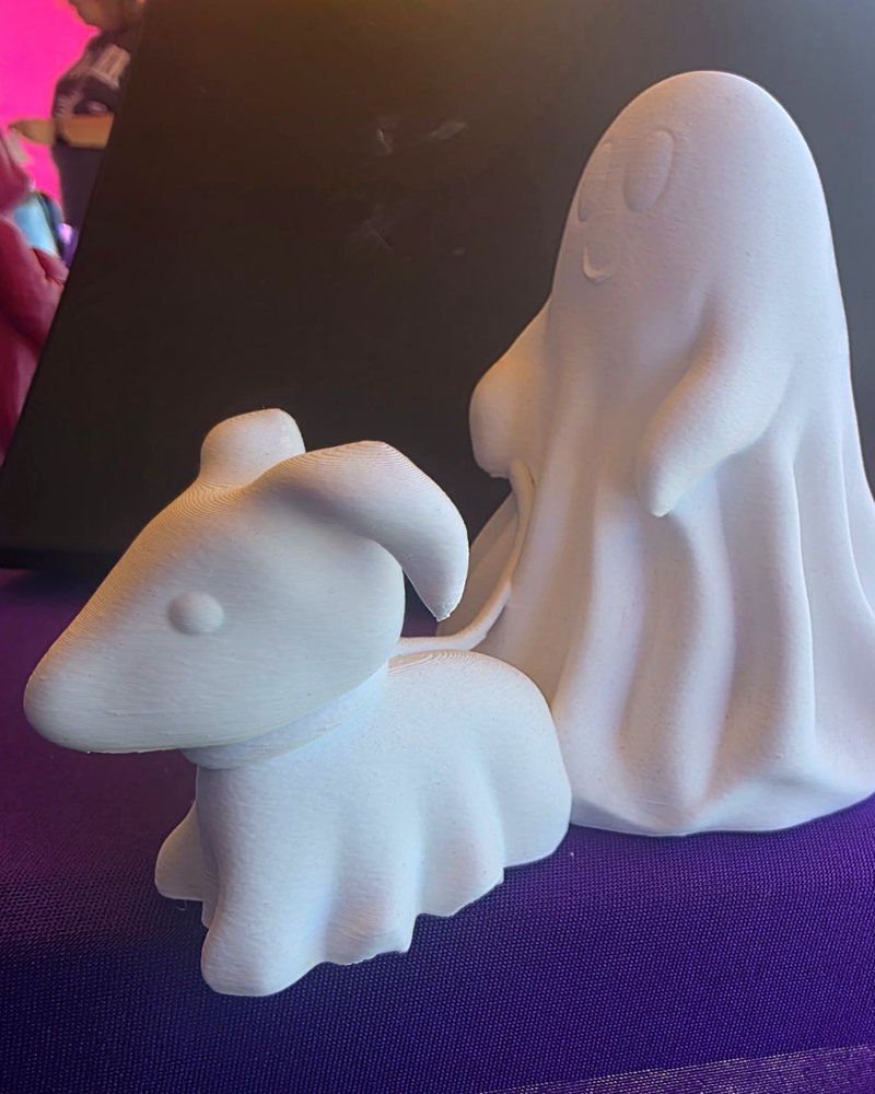 A white ghost in a draped sheet standing next to a smaller ghost dog wearing a sheet.