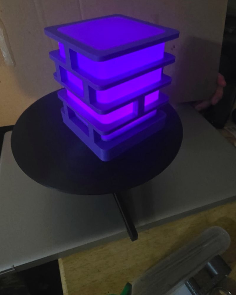 A stacked square tower lamp glowing purple from LED light inside, on a table.