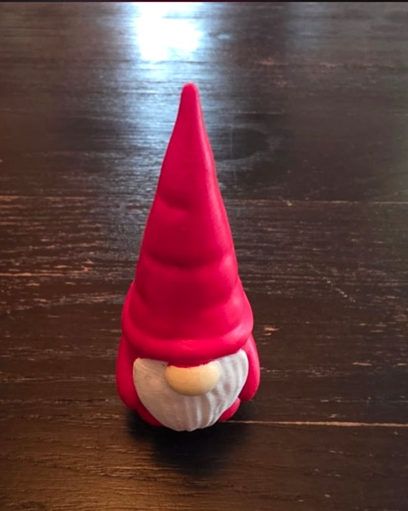 A small red gnome figurine with a pointed hat and white beard, on a wood table.