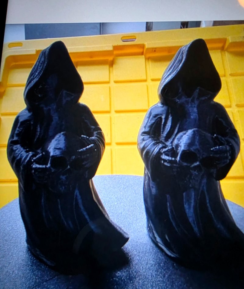 Two black hooded grim reaper figures, each holding a skull.