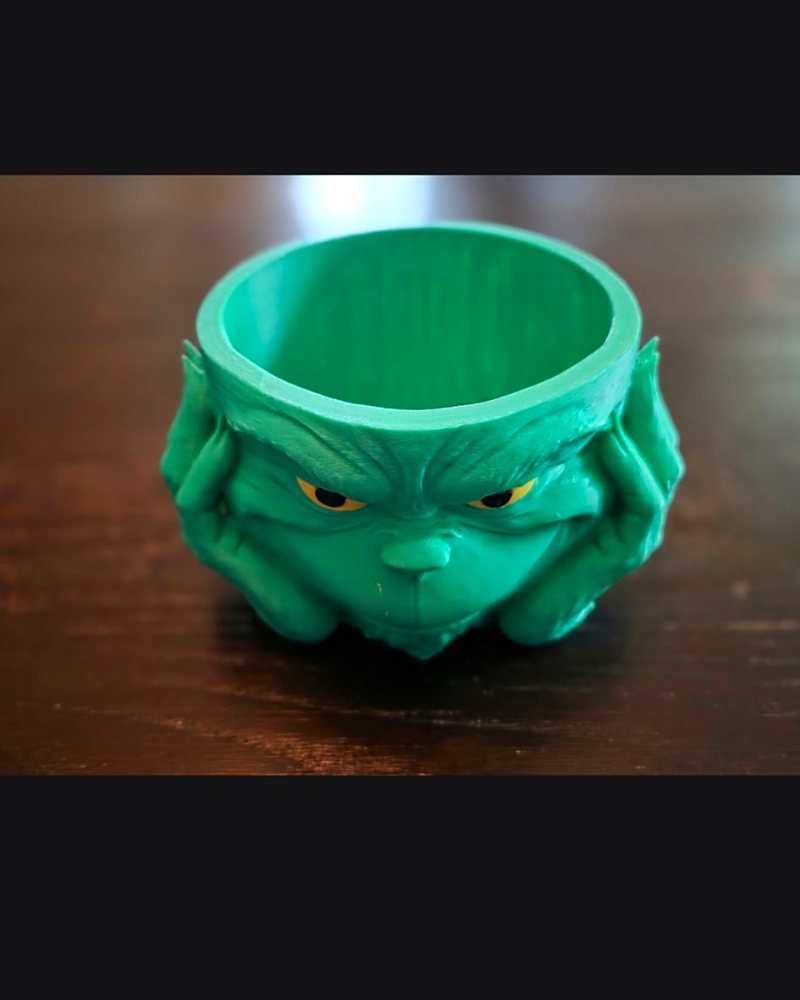 A green Grinch-face bowl with the character's hands under its chin, hollow on top.