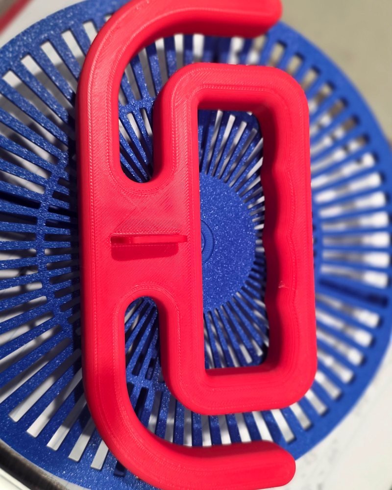 A red looping grocery bag holder handle printed in one piece, shown on a blue slatted plate.
