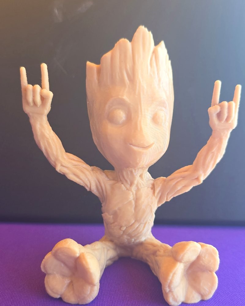 A tan 3D-printed baby tree-creature figure sitting with both hands raised in a rock-on sign.