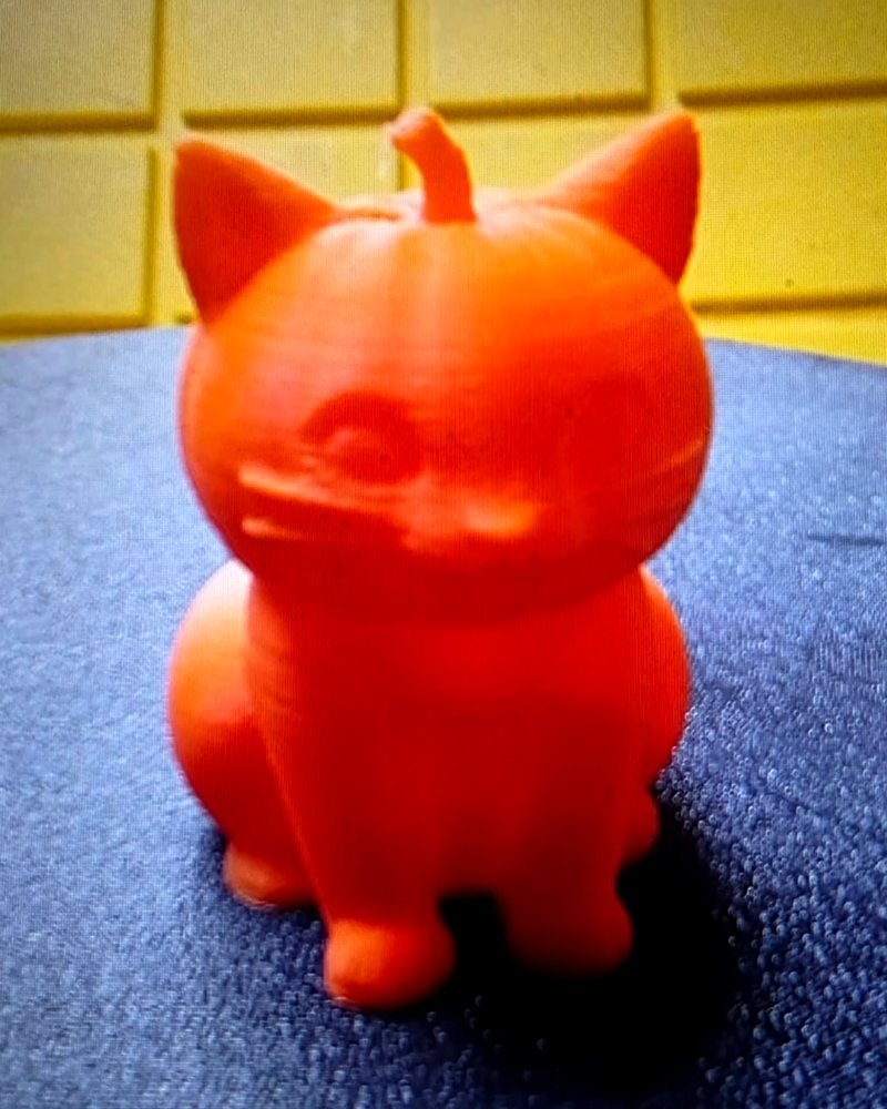A small orange cat figurine with a pumpkin stem on its head.