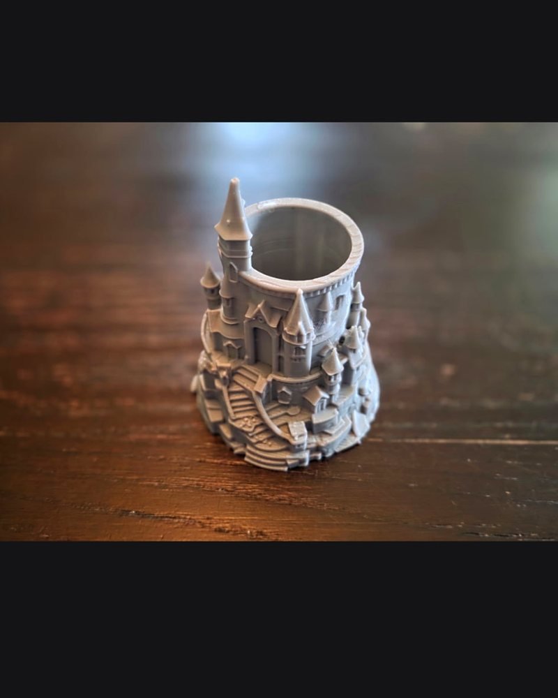 A grey castle-shaped pen holder styled after Hogwarts, with towers and a spiral staircase.