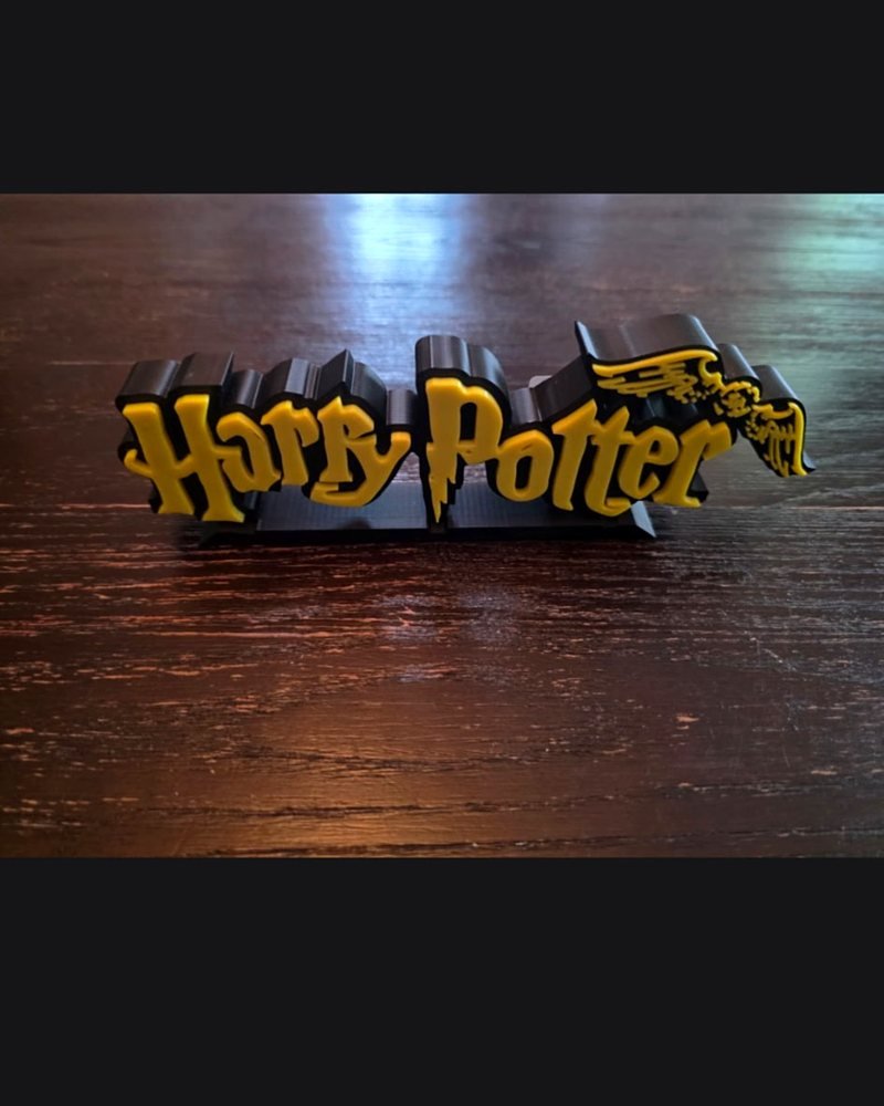 A two-tone yellow and black Harry Potter wordmark sign with a house-crest wing, on a wood table.