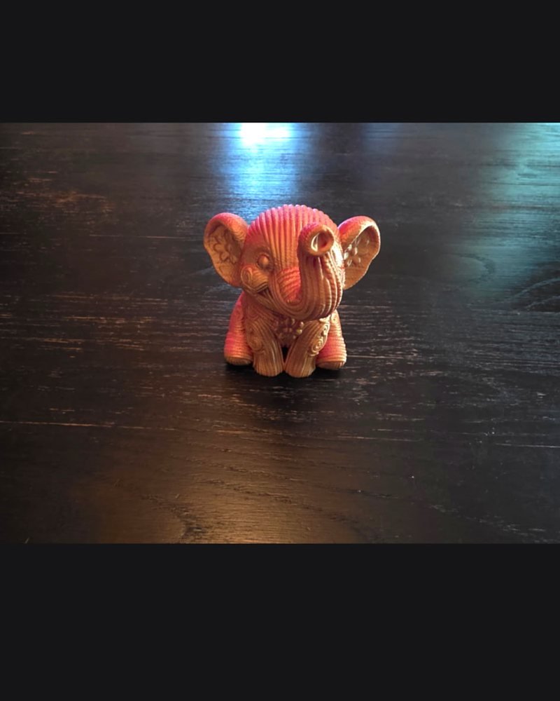 A small pink and cream elephant figurine with a knitted-texture surface, sitting on a wood table.