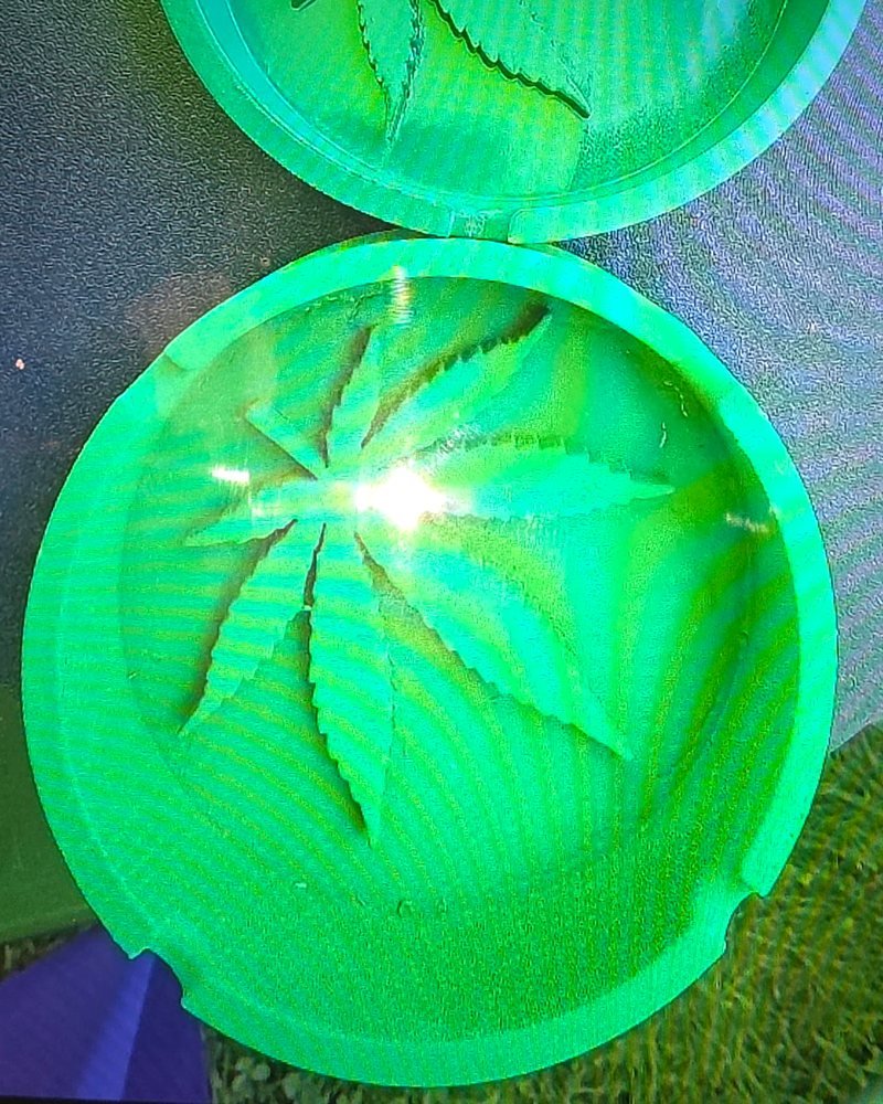 A round two-piece ashtray printed in green, with a leaf pressed into the bottom of each half.