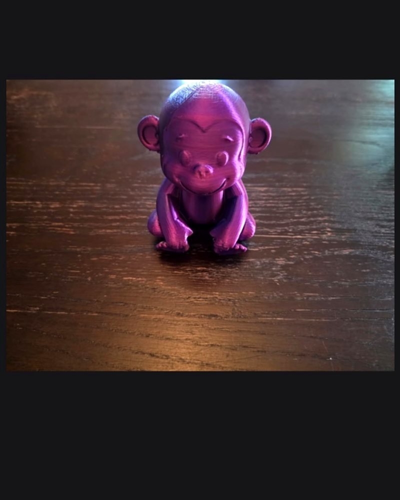 A small purple metallic-sheen monkey figurine sitting on a wood table.