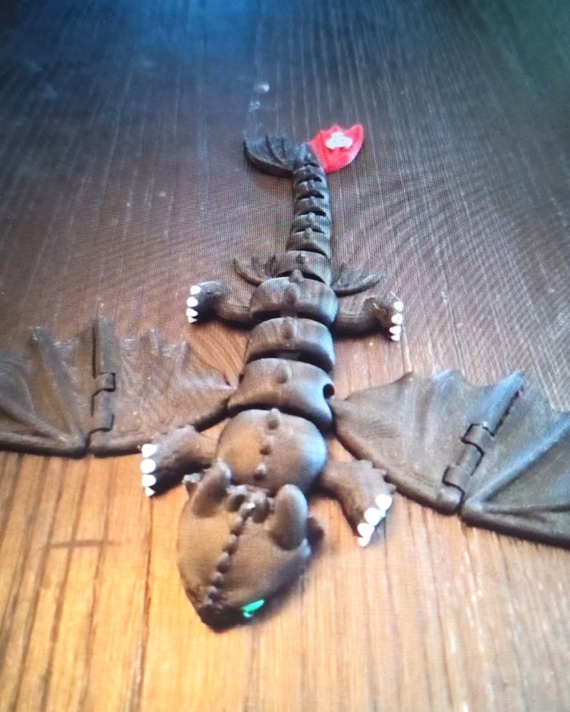 A matte black articulated dragon with folded bat-like wings and a curled tail on a wood floor.