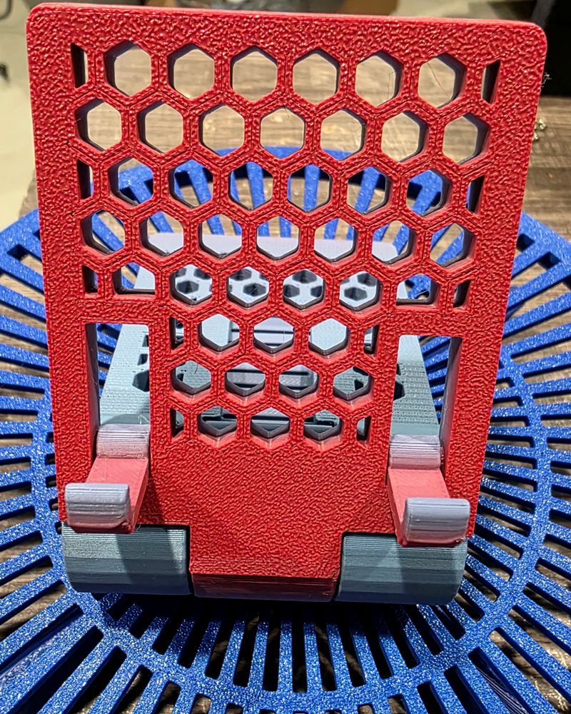 A red honeycomb-patterned phone stand with a gray base, on a blue slatted plate.
