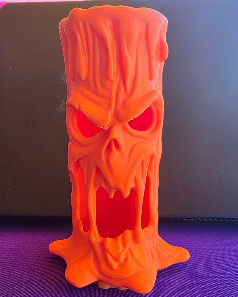 An orange melting-faced pumpkin tower with hollow, red-lit eyes and an open mouth.