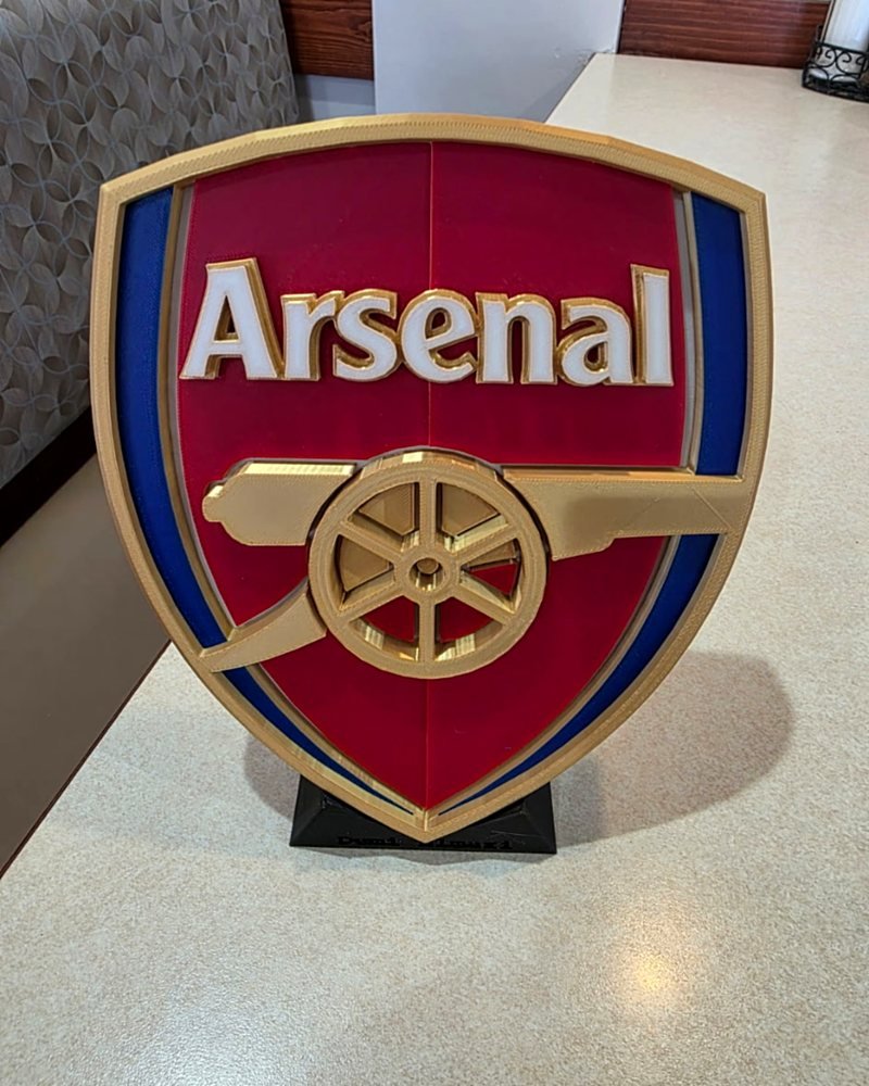 A red, gold, and blue Arsenal crest plaque standing on a small black stand.
