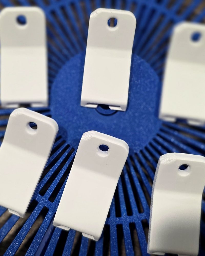 Six white 3D-printed can tab pullers laid out on a blue slatted plate.