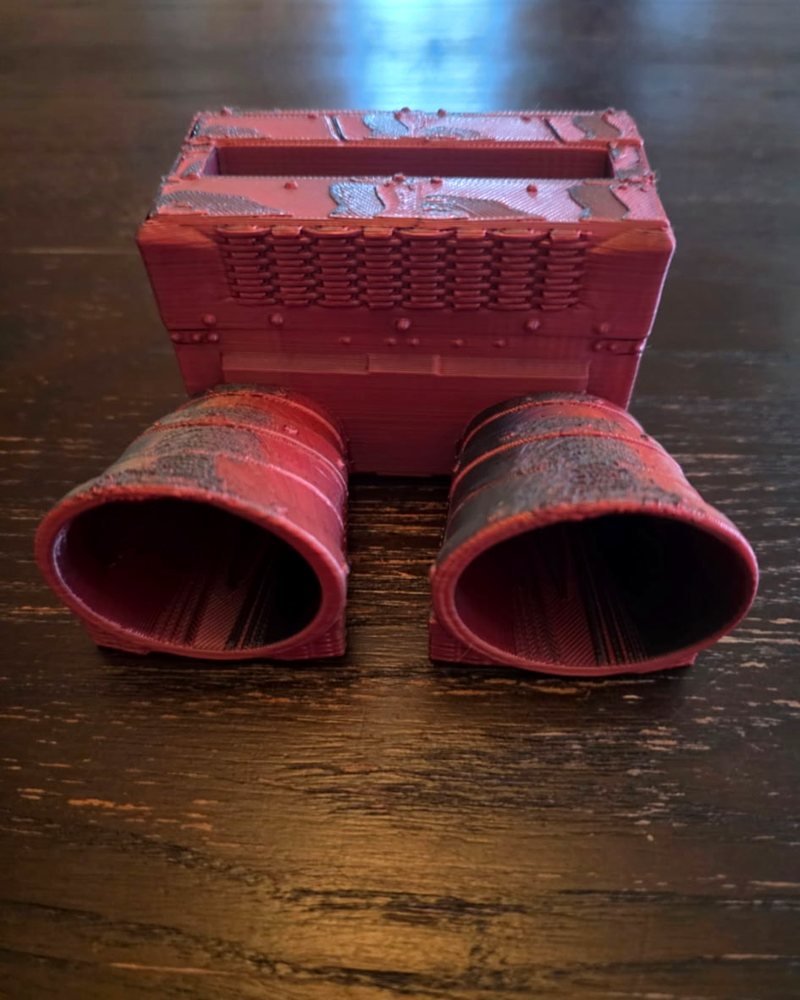 A red 3D-printed speaker amplifier box with a woven grille top and two horn-shaped ports in front.