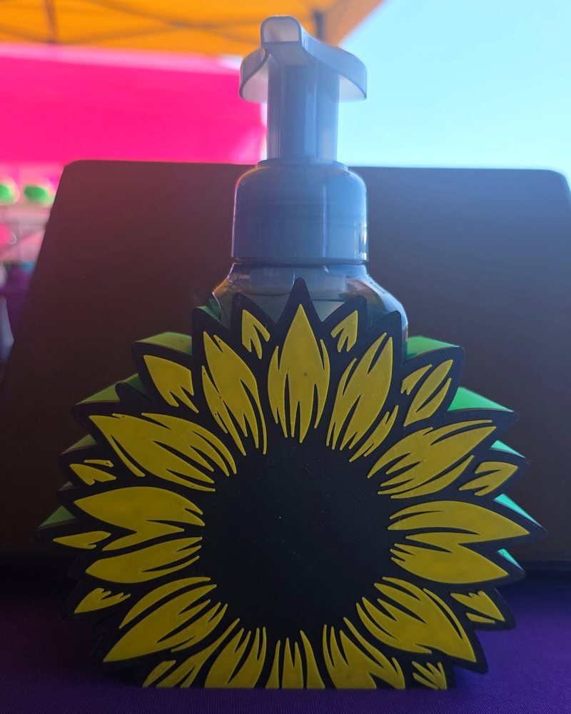 A yellow, black, and green sunflower-shaped holder with a soap bottle standing behind it.