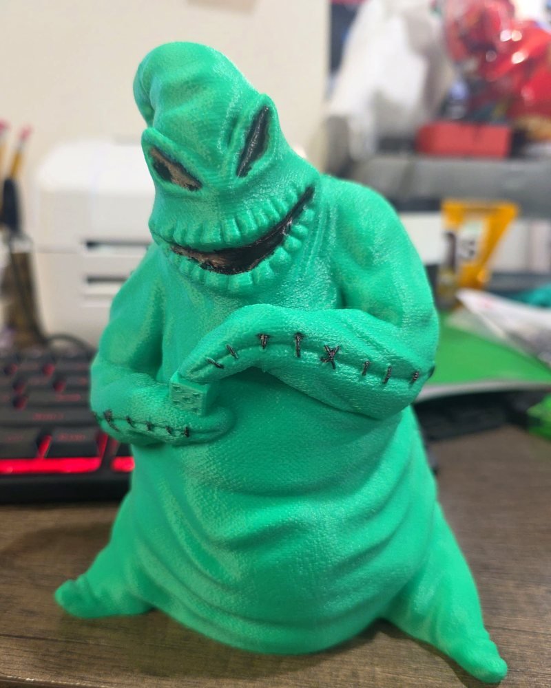 A tall green Oogie Boogie figure with a stitched body and a toothy grin, on a wood desk.