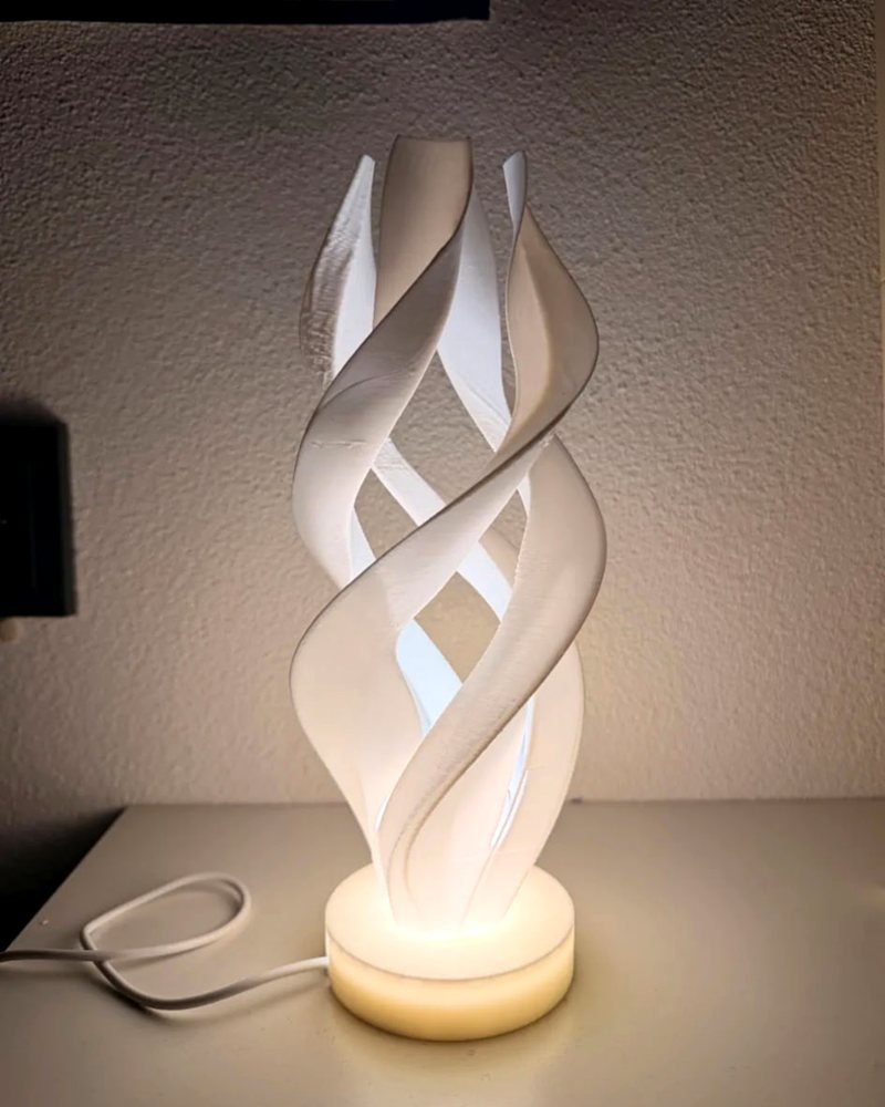 A white spiral ribbon-shaped lamp glowing from an internal light, sitting on a nightstand.